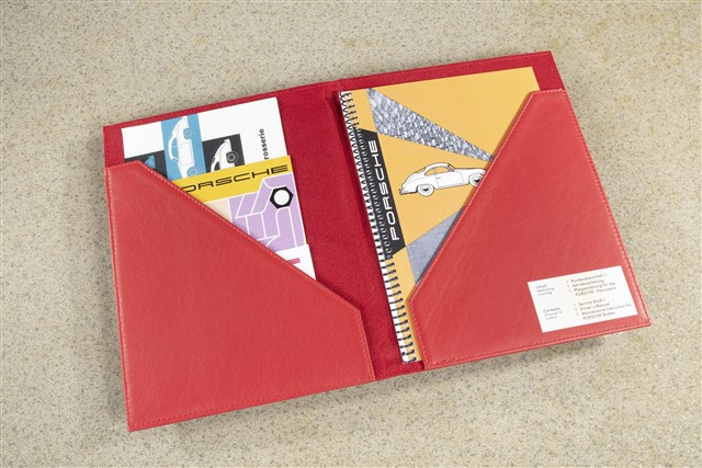 Leder-Dokumentenmappe in Rot mit geprägtem Porsche-Logo zur Aufbewahrung des Servicehefts und der Fahrerhandbücher.